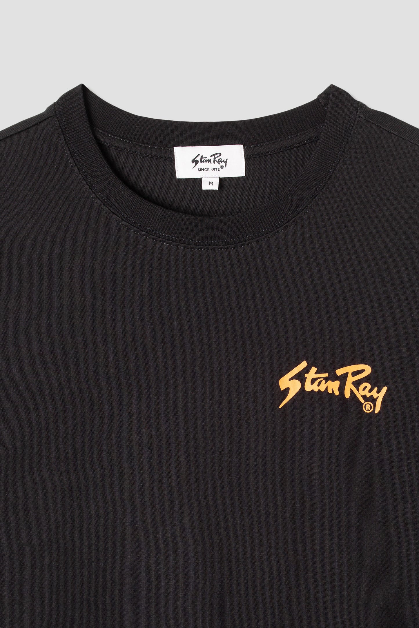 Close-up of Stan OG Tee logo, black with orange print